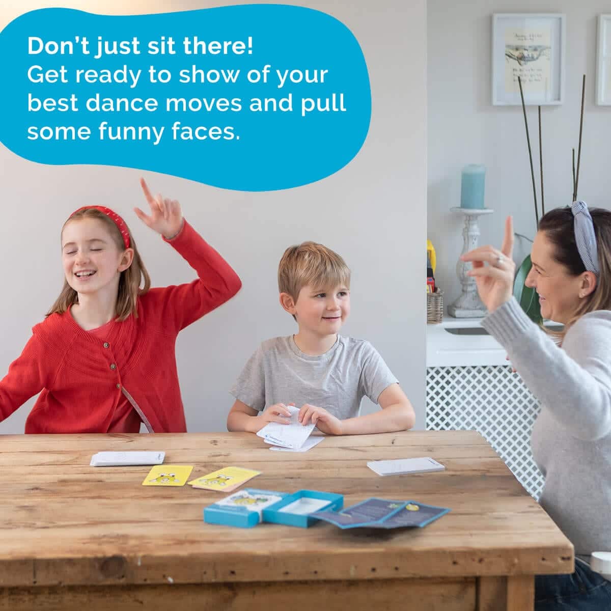 Three children at a table with cards, engaged in an activity, with text encouraging dance and funny faces.